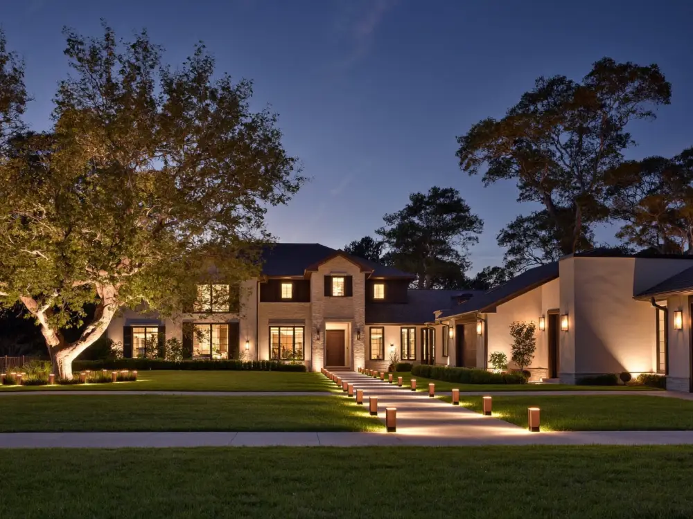 Home at dusk with a run of path lights down the front walk, uplit trees and a warm wash across the facade.