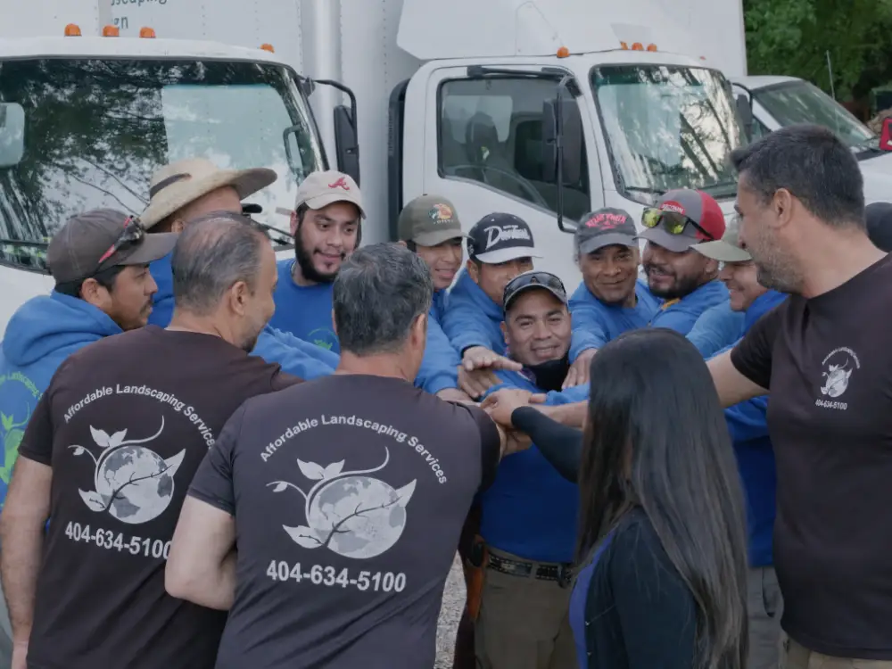 The full ALS crew huddled hands-in in front of the box trucks at the yard, branded shirts and the shop phone number in frame.