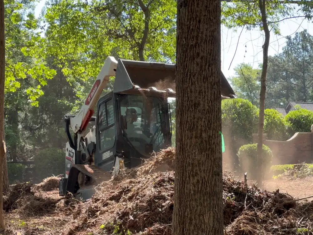 ALS operator clearing a large pile of brush and storm debris with a tracked skid steer at a neighborhood entrance.